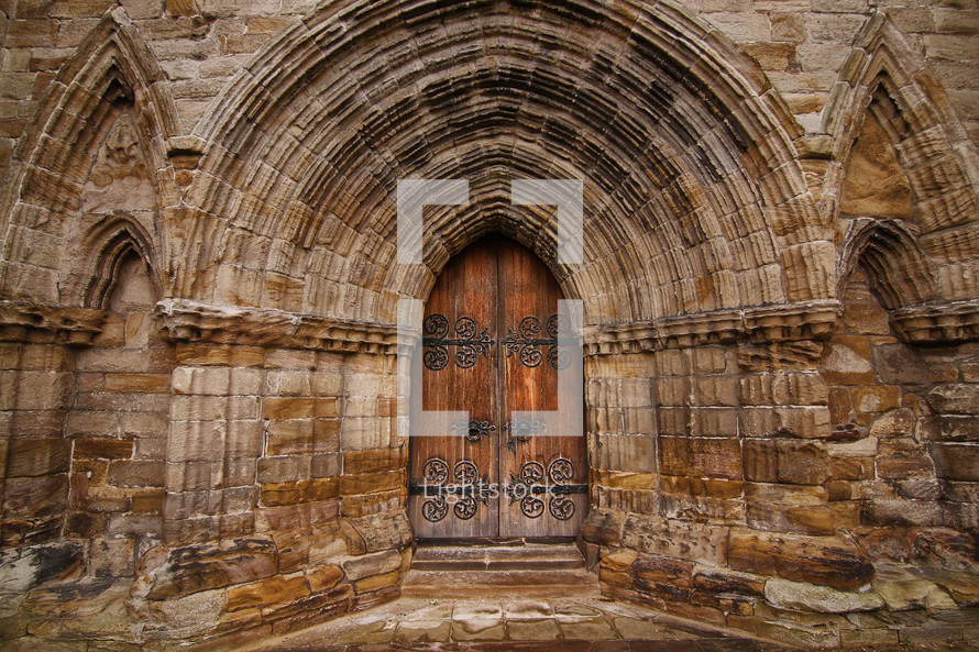 Ornate wooden doorway in the stone arch of an ancient cathedral.