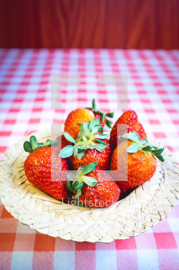 Fresh strawberries decorated on a straw hat. on a red picnic blanket.