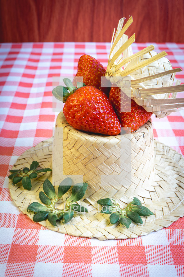 Fresh strawberries decorated on a straw hat. on a red picnic blanket.