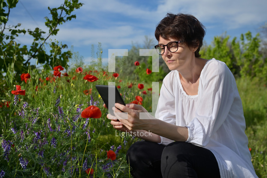 a woman reading a book on a tablet sitting in a field of wildflowers 