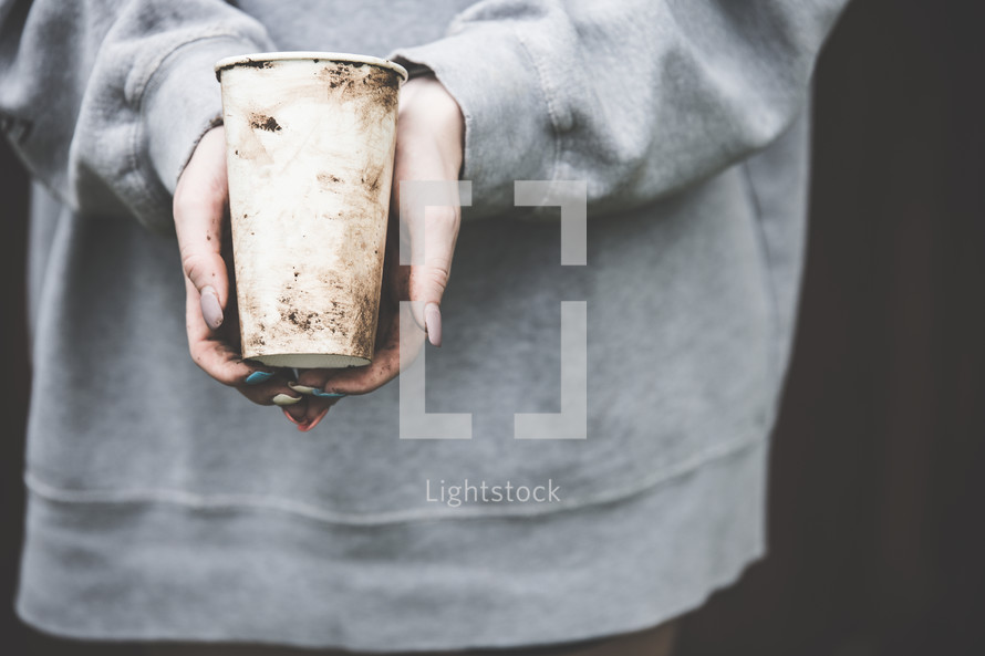 homeless woman with dirty hands holding a cup 