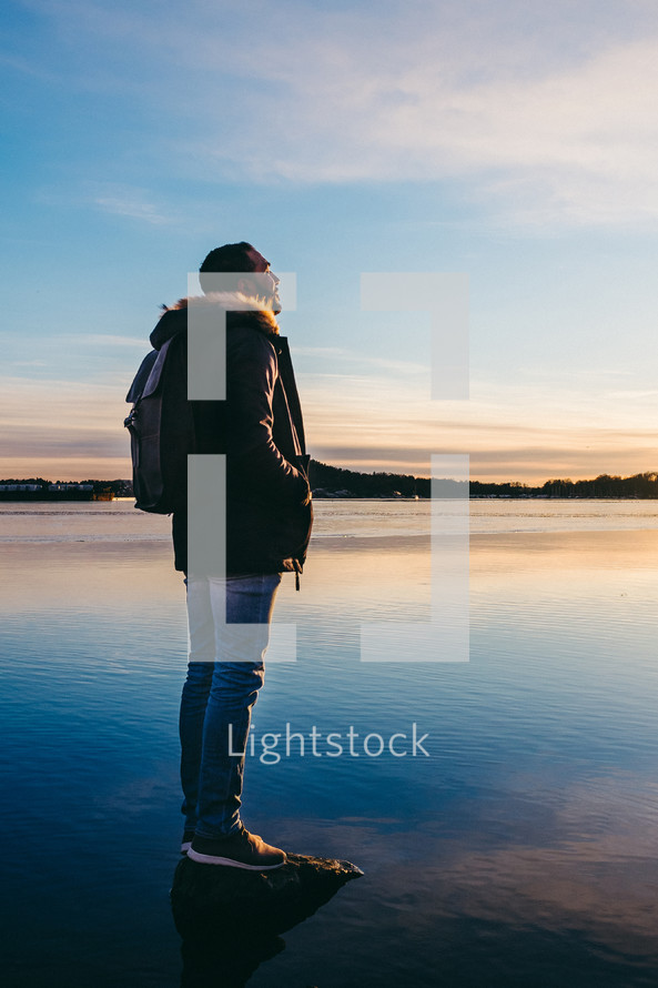 man standing on a stone poking out of a lake 
