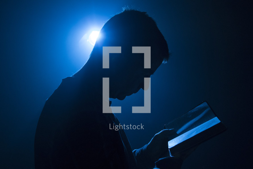 Man holding Bible with light from behind and blue tones