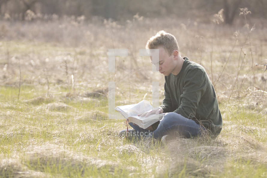 a man sitting in a field reading a Bible 