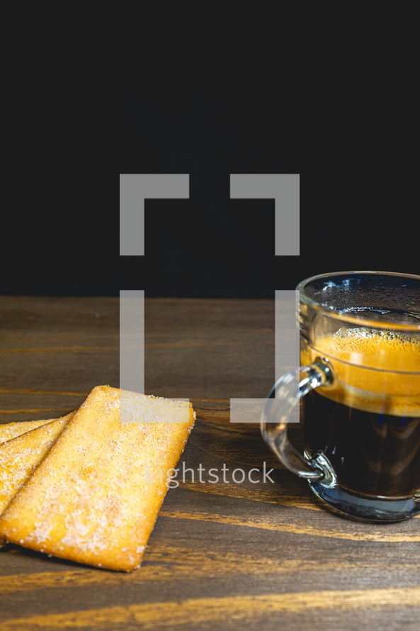 Glass cup of expresso with biscuits on a wooden table.