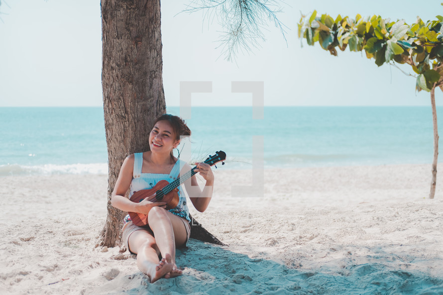 woman playing a ukulele on a beach 