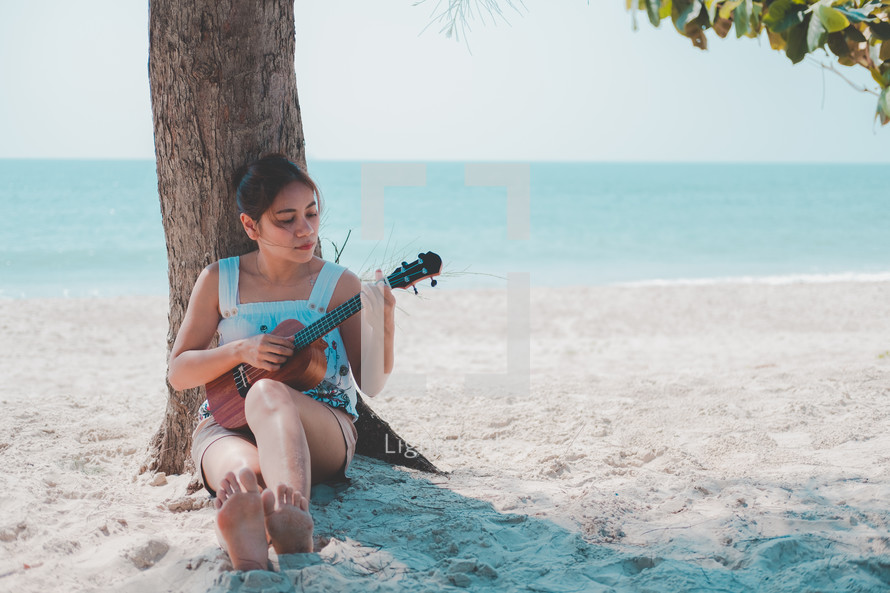 woman sitting on a beach playing a ukulele 