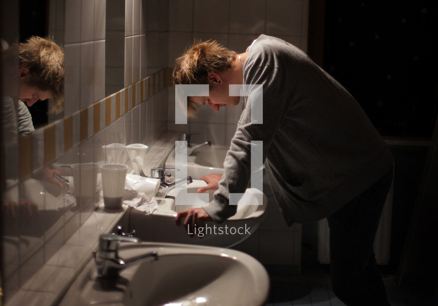 Man leaning over a sink in a bathroom.