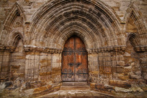 Ornate wooden doorway in the stone arch of an ancient cathedral.