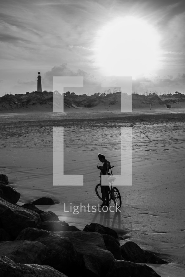 man with a bicycle on a beach and a distant lighthouse