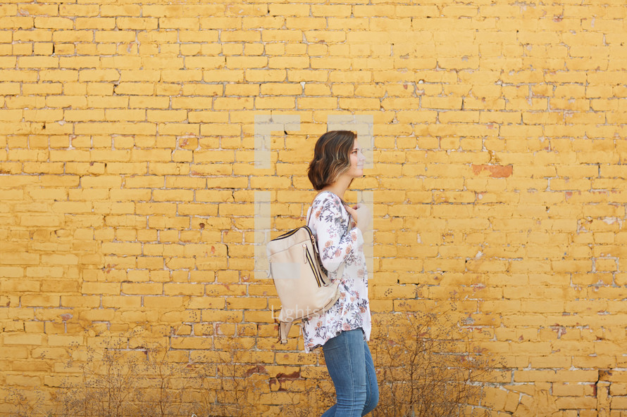 a woman standing in front of a yellow brick wall with her purse 