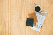 wallet, passport, newspaper, and coffee mug on a table 