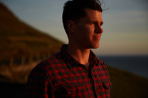 head shot of a man in a plaid shirt standing on a shore 