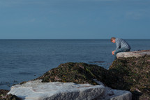 a man sitting on rocks along a shoreline 