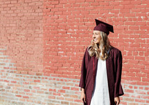 smiling female graduate standing in front of a brick wall 
