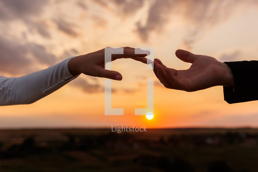 Hands of bride and groom reaching each other, touching fingers on sunset sky countryside background. Helping hands for save and support people concept. Wedding day. Valentine day