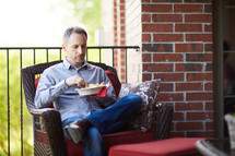 a man sitting on a porch eating a snack 