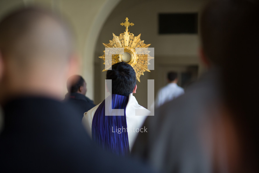 
Priest and a crowd walking during a Catholic Eucharistic procession with a monstrance.
