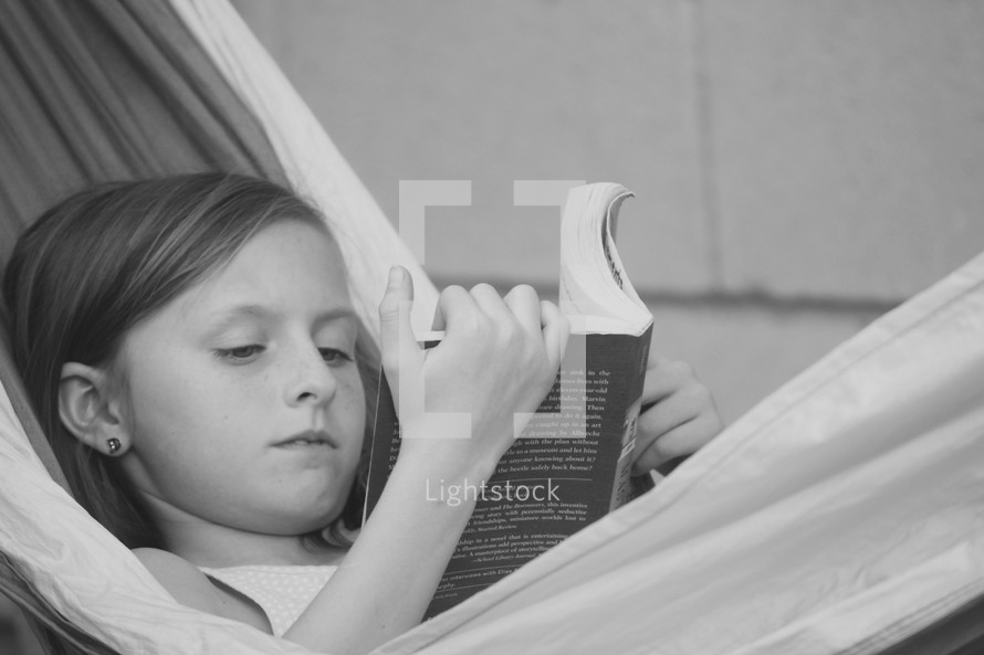 a little girl reading a book in a hammock 