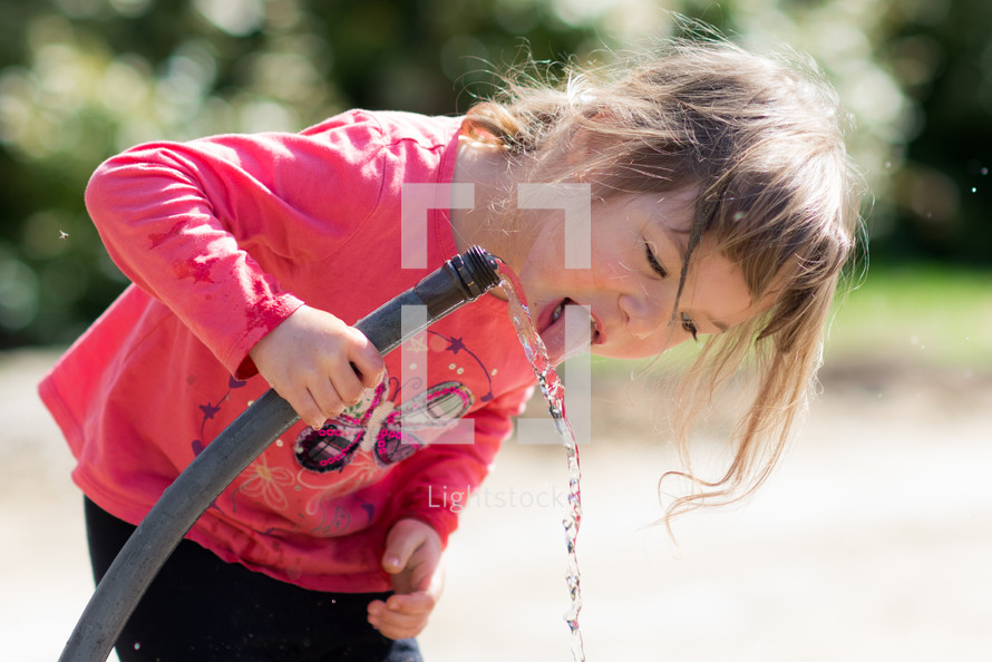 a girl drinking from a water hose