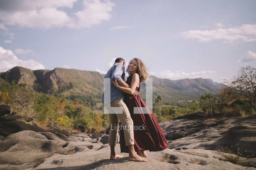 a couple standing on rock in a valley embracing 