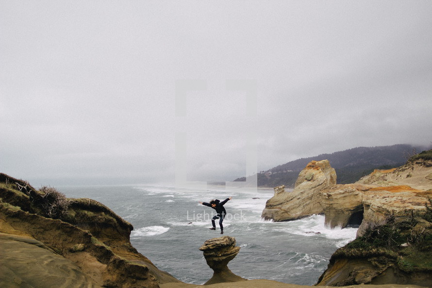 A man jumps in the air on cliffs by the ocean.