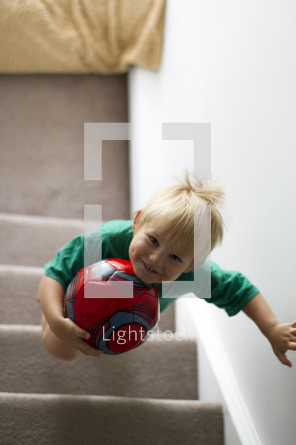 toddler boy walking up steps holding a soccer ball 