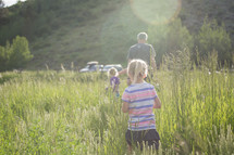 a father and his daughters walking through a field of tall grasses 