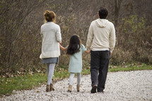 Family walking on a trail outside, holding hands.
