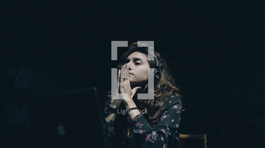 a woman in prayer with headphones sitting in front of a laptop computer 