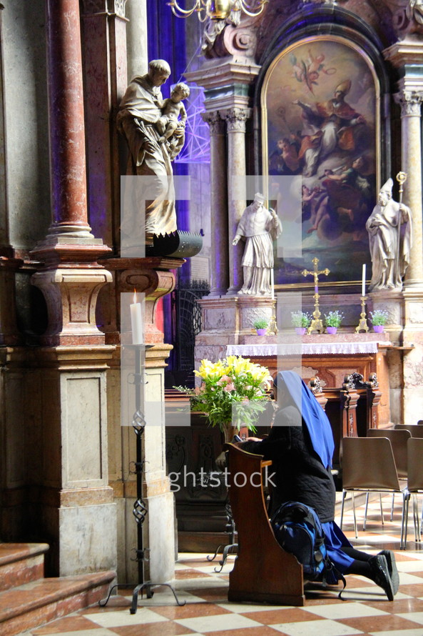 Nun at prayer before a statue of the Mother Mary and baby Jesus in a Catholic Cathedral.