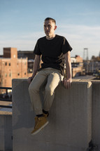 a young man sitting on a concrete wall on the roof of a building 