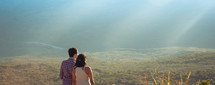man and woman looking at bright sunlight over a valley  