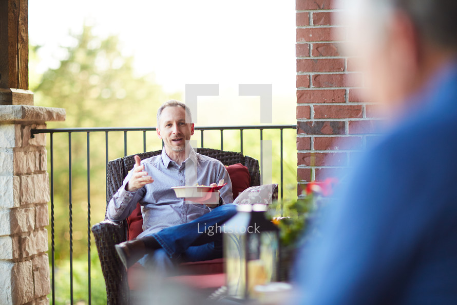 men sitting on a porch eating a snack and talking 