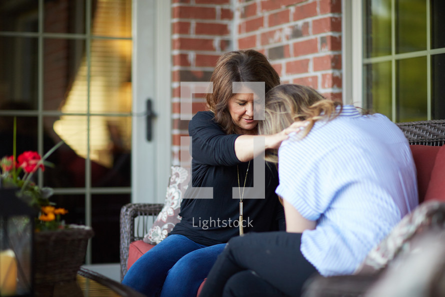 two women holding hands praying on a front porch