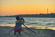 child filming the sunset on a beach 