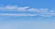 view of mountain peak with sunrise light on top against blue sky with clouds in a foggy day