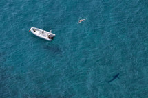 shark circling a boat with a swimmer in the water 