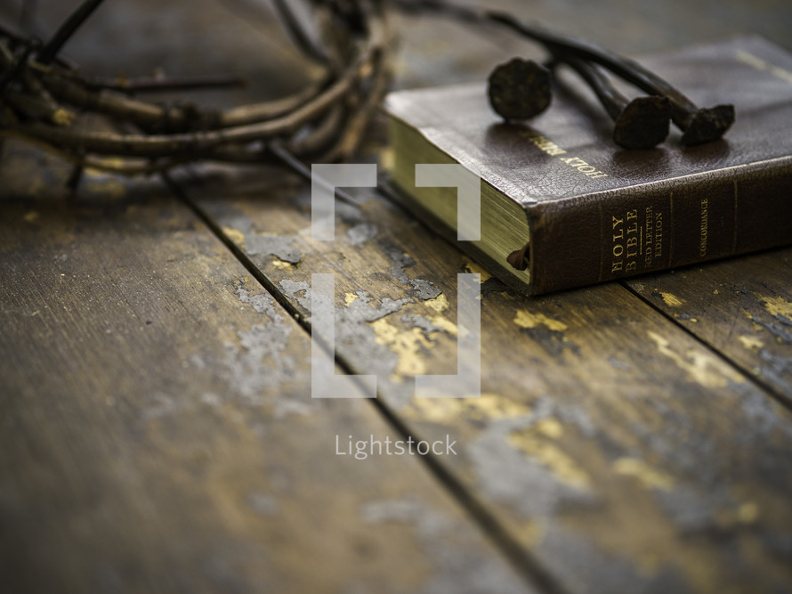 crown of thorns, three nails, and Holy Bible on a wood background 