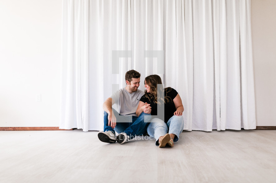 a couple snuggling sitting on the floor of an empty house 