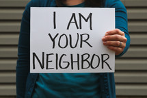 A woman holding a sign that says I am your neighbor