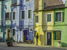 Woman standing outside of yellow home with brightly colored buildings