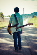 teen boy walking with a guitar on his back 