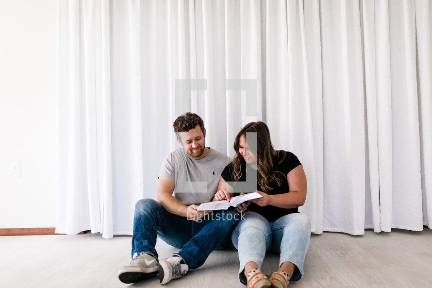 a couple reading a Bible together sitting on the floor 