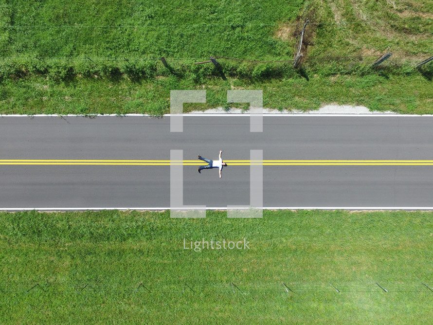 man lying in the middle of a road from overhead 
