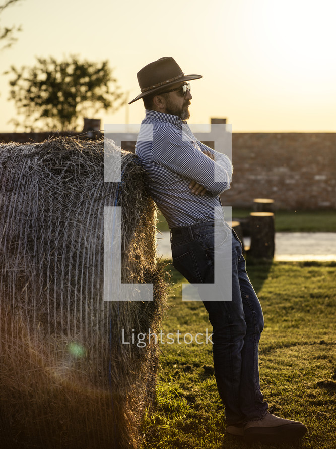 man on a farm leaning against a hay bale 