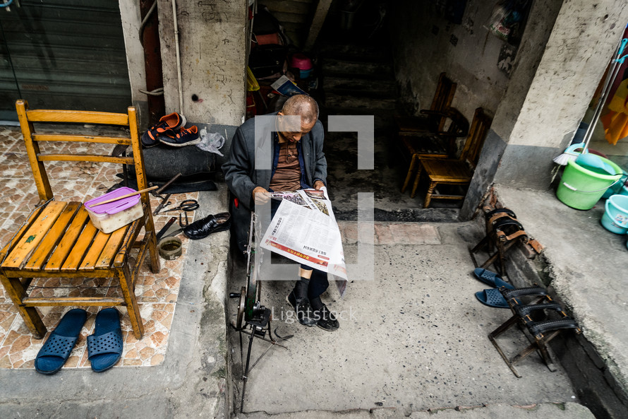 man reading a newspaper on a sidewalk in China 