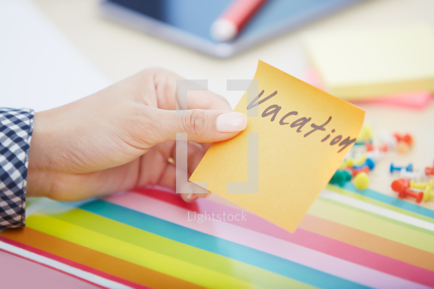 woman holding a sticky note with the word vacation on it 