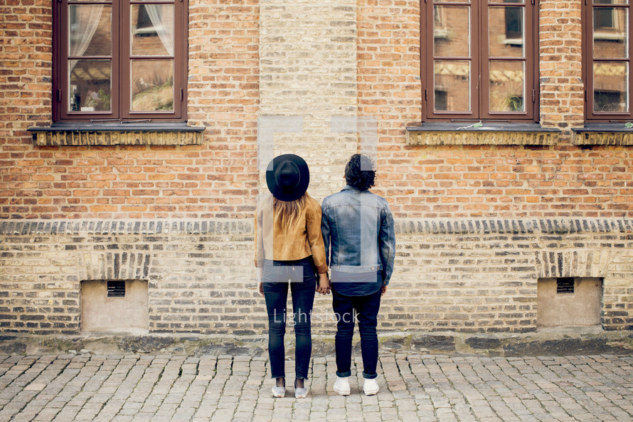Couple holding hands standing in front of a brick building.