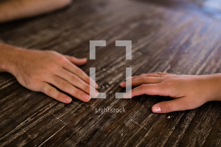 hands of a couple on a wooden table 